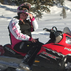 Photo of a girl siting on a red snowmobile with snow and trees in the background